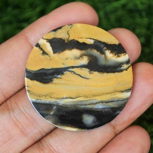 May include: A round, yellow and black agate cabochon with a swirling pattern. The cabochon is about 2 inches in diameter.