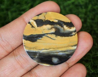 Könnte beinhalten: Ein runder, gelber und schwarzer Achat-Cabochon mit einem wirbelnden Muster. Der Cabochon hat einen Durchmesser von etwa 5 cm.