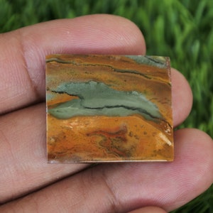 May include: A square-shaped, polished, green, brown, and orange jasper cabochon with a unique pattern.