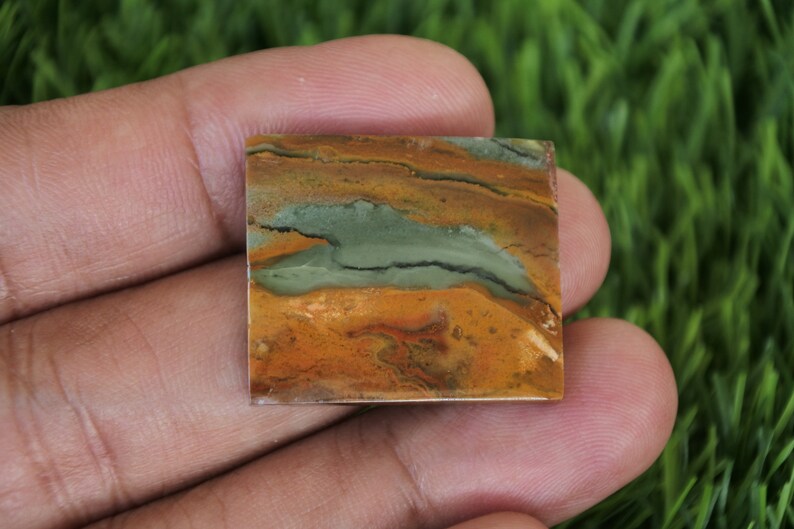 May include: A square-shaped, polished, green, brown, and orange jasper cabochon with a unique pattern.