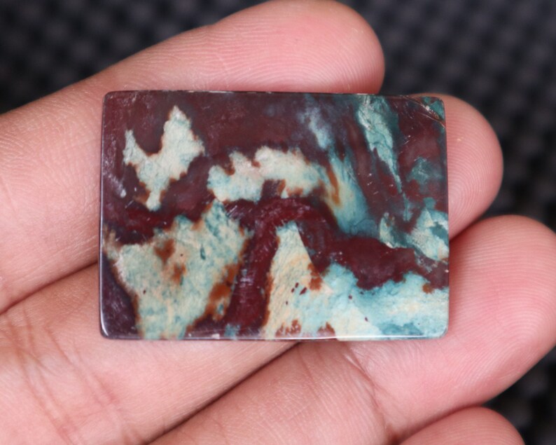 May include: A rectangular, polished stone with a swirling pattern of red, white, and blue colors. The stone has a smooth, polished surface and is suitable for jewelry making or crafting.