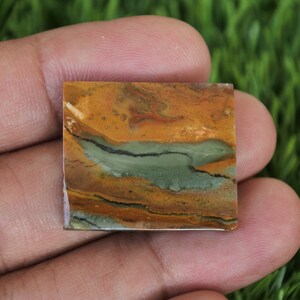 May include: A square-shaped, polished stone with a layered pattern of brown, orange, and green colours. The stone has a smooth, polished surface.