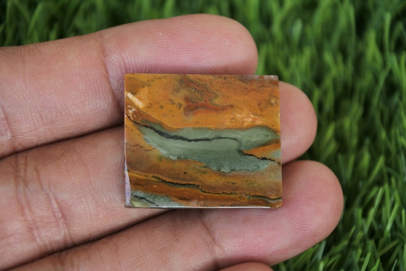 May include: A square-shaped, polished stone with a layered pattern of brown, orange, and green colours. The stone has a smooth, polished surface.