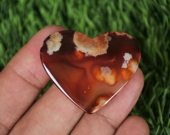 Puede incluir: Un ágata de cornalina en forma de corazón con patrones marrones y blancos. El ágata está pulida y lisa.