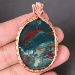 Peut inclure: Un pendentif en fil de cuivre enveloppé avec une pierre à motifs verts, rouges et blancs.