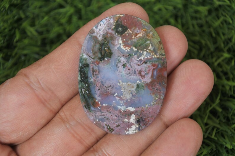 May include: A polished oval cabochon of green, pink, and white agate with a swirling pattern. The stone has a high polish and is translucent.