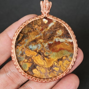 Peut inclure: Un pendentif en fil de cuivre enveloppé avec une pierre d'agate ronde multicolores avec des tourbillons bruns, jaunes, rouges et blancs.