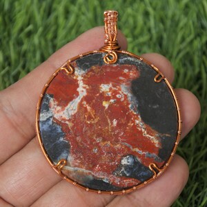 Peut inclure: Un pendentif en fil de cuivre enveloppé avec une pierre d'agate ronde rouge, noire et blanche.