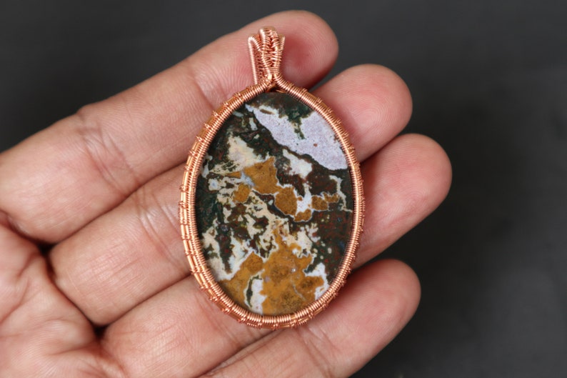 May include: A copper wire wrapped pendant featuring a colourful agate stone with brown, white and yellow patterns.