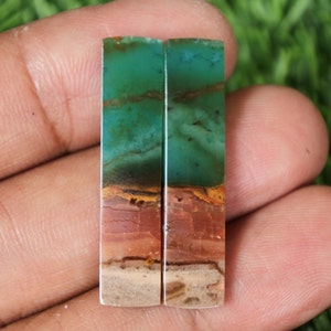 May include: Two rectangular green, brown and white gemstone cabochons. The cabochons are approximately 5 cm long and 1.25 cm wide.