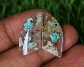 Op de afbeelding: Twee heldere, doorschijnende cabochons met een uniek, gevlekt patroon van witte, bruine en blauwgroene insluitsels. De cabochons zijn traanvormig en hebben een glad, gepolijst oppervlak.