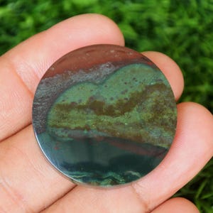 May include: A round, green, brown, and black stone cabochon with a swirling pattern. The stone is approximately 1 inch in diameter.