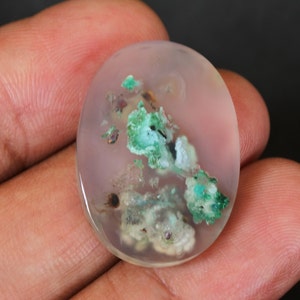 May include: A translucent white oval cabochon with green and white inclusions. The cabochon is approximately 2.5 cm in diameter.