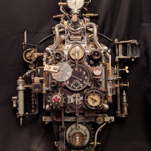 May include: A steampunk-style clock with multiple gears, dials, and gauges. The clock face has Roman numerals and a red star. The clock is made of metal and has a distressed finish.