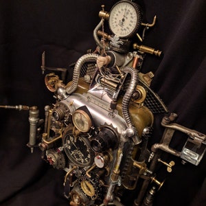 May include: A steampunk-style clock with multiple gears, dials, and gauges. The clock has a silver face with black markings and a gold-colored frame. The clock is attached to a variety of pipes and other metal objects.