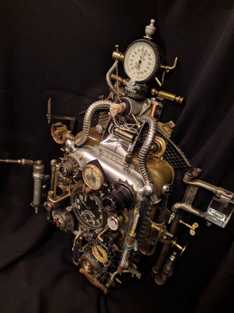 May include: A steampunk-style clock with multiple gears, dials, and gauges. The clock has a silver face with black markings and a gold-colored frame. The clock is attached to a variety of pipes and other metal objects.
