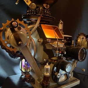 Puede incluir: Una cabeza de robot de estilo steampunk con una luz naranja incandescente, engranajes, cadenas y varias piezas metálicas. La cabeza del robot está unida a una base con una variedad de indicadores y otros componentes mecánicos.