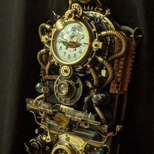 Puede incluir: Un reloj de pared de estilo steampunk con una esfera crema, n&uacute;meros negros y un emblema de ave estilizado. El reloj est&aacute; encerrado en una compleja disposici&oacute;n de engranajes, tubos y medidores de lat&oacute;n, con un elemento de vidrio verde en la parte superior. El dise&ntilde;o es intrincado e industrial.