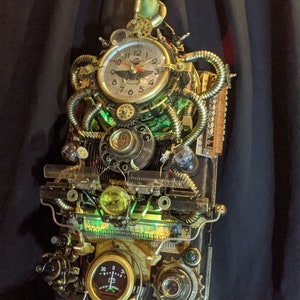 Puede incluir: Reloj de pared estilo steampunk con acabado en lat&oacute;n y cobre. El reloj presenta una esfera redonda con n&uacute;meros romanos, engranajes, tubos y medidores. Luces verdes iluminan el interior, creando una est&eacute;tica industrial &uacute;nica.