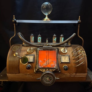 Op de afbeelding: Een steampunk-stijl klok met een houten basis, messing accenten en een kompas. De klok heeft een digitaal display met vier cijfers en een klein venster met een rood en oranje beeld. De klok staat op een messing basis met drie poten.