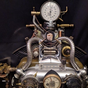 May include: A steampunk-style clock with a silver and brass finish. The clock has a variety of gears, pipes, and gauges, including a pressure gauge with the text "000200" and a smaller gauge with the text "20 30 40 50".