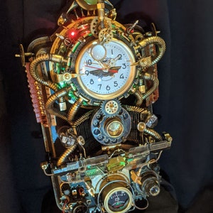 Puede incluir: Un reloj de estilo steampunk con una esfera blanca, engranajes dorados y tuber&iacute;as de cobre. El reloj tiene una est&eacute;tica vintage con detalles intrincados, incluyendo un medidor y elementos decorativos. El reloj est&aacute; iluminado con luces verdes y rojas.