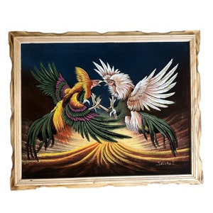 May include: A framed velvet painting of two roosters fighting. The roosters are in a dynamic pose, with their wings spread and their beaks open. The background is a dark blue with a golden yellow and orange landscape. The painting is signed "Sanchez" in the lower right corner.