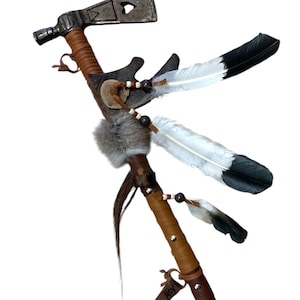 May include: A brown leather-wrapped tomahawk with a metal head and feathers. The tomahawk has a small fur pom-pom and a leather tag with the word "Next" written on it.