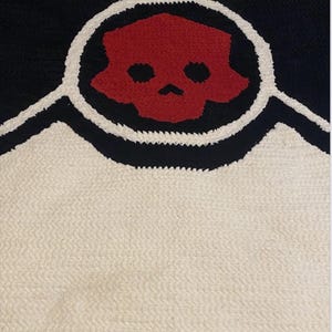 May include: A black, white, and red skull design rug. The rug features a red skull within a white circle, outlined in black, set against a black background. The lower portion is white.
