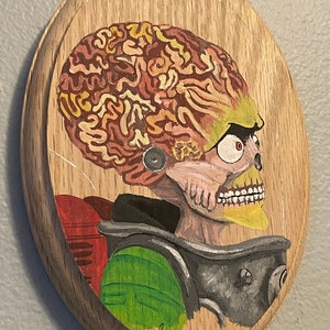 May include: A hand-painted wooden plaque featuring a detailed portrait of an alien with a large brain, yellow teeth, and a red eye. The alien is wearing a green and gray spacesuit. The plaque is signed "Mike '23".