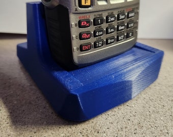May include: A blue plastic charging stand for a silver two-way radio with a keypad and a screen. The radio has the text "WIRES-X" and "TX PWR" on it.