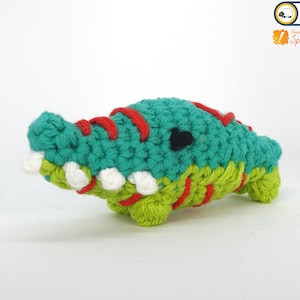 May include: A crocheted alligator toy with green, red, and white yarn. The alligator has a black eye and a toothy grin.