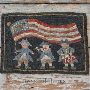 Puede incluir: Alfombra hecha a mano con un diseño patriótico que muestra una bandera estadounidense y tres figuras con vestimenta colonial. La alfombra tiene un fondo oscuro con detalles en rojo, blanco y azul. El texto "tweedful things" está en la parte inferior.