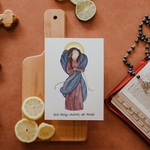 May include: A watercolor illustration of a figure with a halo, wearing a pink dress and blue shawl, with the text "Our Lady Undoer of Knots." The image is on a white background, with a wooden cutting board, lemons, and a rosary in the background.