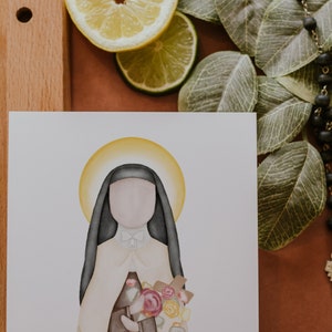 Puede incluir: Una ilustraci&oacute;n de acuarela de una mujer con un h&aacute;bito blanco y negro y un halo. Ella sostiene un ramo de flores rosas, amarillas y blancas. El fondo es blanco.