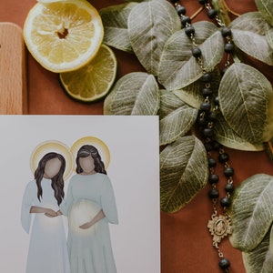 May include: A white card with a watercolour illustration of two women standing side-by-side. The woman on the right is pregnant and holding her belly. Both women have halos around their heads.
