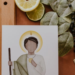 May include: A watercolor illustration of a saint with a halo, holding a staff. The saint is wearing a green robe and a white tunic. The background is white.