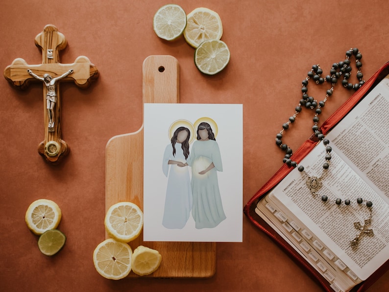 May include: A print depicting two women in white and green robes, standing side by side. The woman on the left is holding the hand of the woman on the right, who is pregnant. The print is on a wooden chopping board, with a crucifix and a rosary in the background.