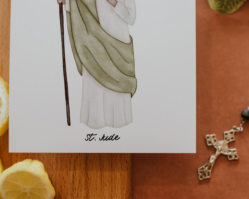 May include: A watercolor illustration of a saint holding a staff. The saint is wearing a white robe with a green cloak. The illustration is on a white background with the text "St. Jude" written below.