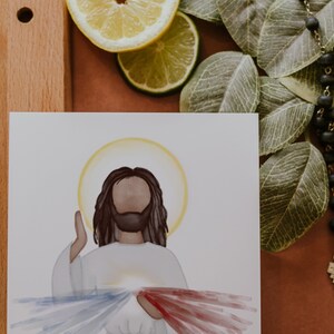 May include: A watercolor painting of Jesus Christ with a halo, wearing a white robe and raising his right hand. The painting depicts the Divine Mercy image with red and blue rays emanating from his chest.