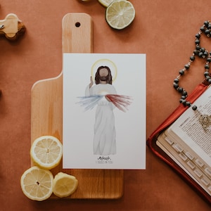 May include: A watercolor painting of Jesus Christ with a red and blue heart and rays of light emanating from it. The text below reads "Jesus, I trust in you".