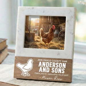May include: A marble and wood picture frame featuring a photograph of a brown chicken in a barn. The frame includes the text "2026 PASCO COUNTY FAIR ANDERSON AND SONS" and "Thank you for supporting my project. -Mason Ross."