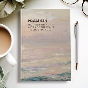 Pode incluir: Um diário de capa dura com um design abstrato com tema oceânico em cores pastel. A capa apresenta o texto "PSALM 93:4" e uma citação. Uma caneta prateada e óculos estão ao lado do diário, e uma xícara de café está no canto superior esquerdo.