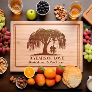 Könnte beinhalten: Ein rechteckiges Schneidebrett aus hellem Holz mit einer Lasergravur eines Weidenbaums und zwei Personen auf einer Schaukel. Der Text lautet 9 YEARS OF LOVE und David and Colleen. Umgeben von Weintrauben, Nüssen und verschiedenen Früchten.
