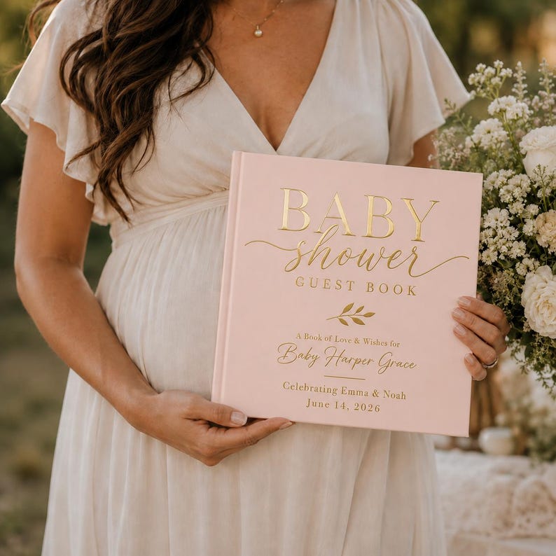 May include: A square baby shower guest book with a light pink cover and gold foil lettering. The text reads BABY shower GUEST BOOK, A Book of Love & Wishes for Baby Harper Grace, Celebrating Emma & Noah, and the date June 14, 2026, with a leaf icon.