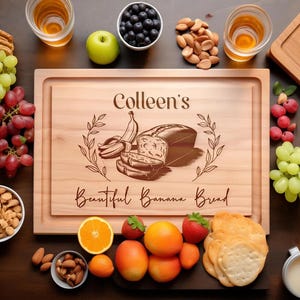 May include: A rectangular wooden cutting board engraved with the text Colleen's Beautiful Banana Bread, featuring an illustration of a banana and a loaf of bread, surrounded by grapes, nuts, berries, orange slices, and crackers.