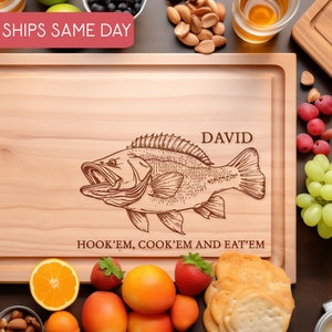 May include: Personalised wooden chopping board with a fish illustration and the text "HOOK'EM, COOK'EM AND EAT'EM". The board is engraved with the name "DAVID".