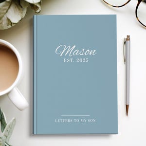 以下が含まれることがあります： 「Mason EST. 2025」と「Letters to My Son」の文字が書かれた薄い青色のジャーナル