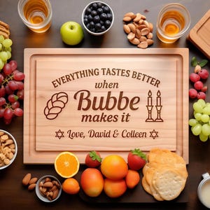 May include: A rectangular wooden cutting board engraved with the text "EVERYTHING TASTES BETTER when Bubbe makes it" and "Love, David & Colleen," featuring illustrations of a challah bread, two candlesticks, and two Stars of David.