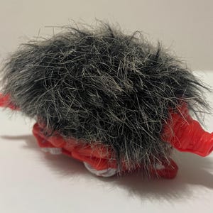 Könnte beinhalten: Ein rotes und weißes Spielzeugwesen mit einem zotteligen, grauen fellartigen Kopf. Das Spielzeug hat rote Hörner und Füße. Das Wesen liegt auf der Seite.